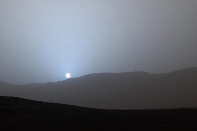 В полдень небо Марса желто-оранжевое. причина таких отличий от цветовой гаммы земного неба - свойства тонкой, разреженной, содержащей взвешенную пыль атмосферы Марса. На Марсе рэлеевское рассеяние лучей (которое на Земле и является причиной голубого цвета неба) играет незначительную роль, эффект его слаб, но проявляется в виде голубого свечения при восходе и закате Солнца, когда свет проходит более толстый слой воздуха.  На фото - Марсианский закат, 15 апреля 2015 года. 